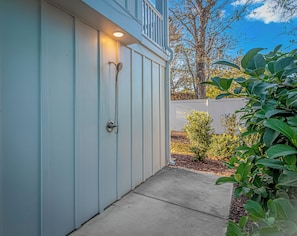 A light blue exterior wall with a door, a small porch area, and a garden with various plants.