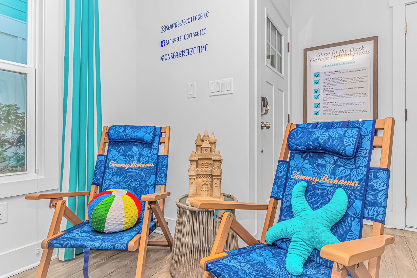 Zwei strandbezogene Stühle mit Kissen, ein Strandball und ein Sandburgenmodell in einem Zimmer mit weißer Wand und einer Tür.
