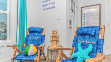 Zwei strandbezogene Stühle mit Kissen, ein Strandball und ein Sandburgenmodell in einem Zimmer mit weißer Wand und einer Tür.