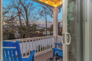 A covered outdoor area with a glass door, blue chairs, and a bottle of wine on a table.