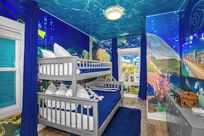 Una habitación con literas, una ventana y un mural de escenas submarinas.
