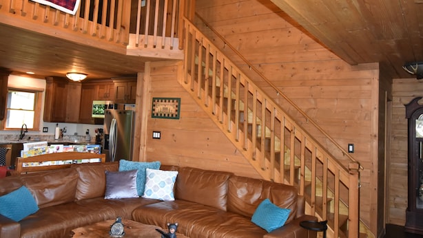 A wooden cabin interior with a brown leather couch, a wooden staircase, and a kitchen area. - Amazing Views!! Creekside Cabin, Wrap Around Porch, Close to Town! Dogs Welcome! (Hiawassee)
