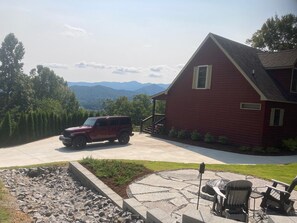 A red house with a driveway, a stone patio with outdoor furniture, and a view of mountains in the background. - Amazing Views!! Creekside Cabin, Wrap Around Porch, Close to Town! Dogs Welcome! (Hiawassee)