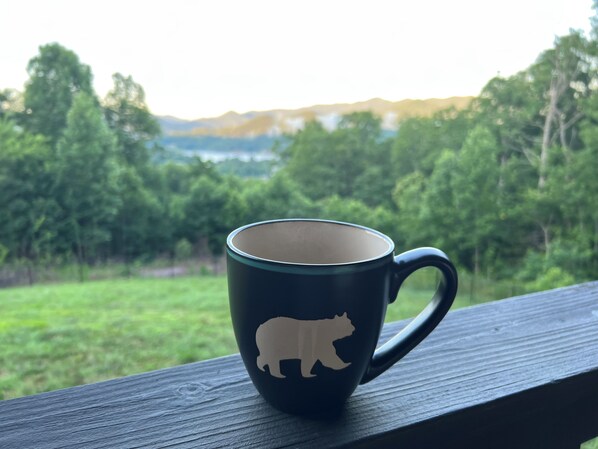 A mug with a bear silhouette on a wooden surface with a view of a forest and hills in the background. - Amazing Views!! Creekside Cabin, Wrap Around Porch, Close to Town! Dogs Welcome! (Hiawassee)
