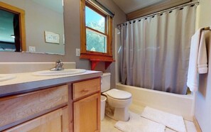 A bathroom with a wooden vanity, a white sink, a toilet, and a bathtub with a curtain. - Amazing Views!! Creekside Cabin, Wrap Around Porch, Close to Town! Dogs Welcome! (Hiawassee)