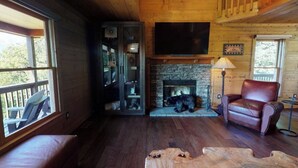 A cozy cabin interior with a stone fireplace, leather armchair, and a large TV mounted on the wall. - Amazing Views!! Creekside Cabin, Wrap Around Porch, Close to Town! Dogs Welcome! (Hiawassee)
