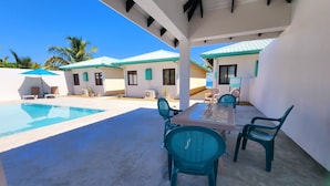 A covered outdoor area with a pool, seating, and a building with a green roof. - Tropical 1 Bedroom Cabana on Private Oasis (Maya Beach)