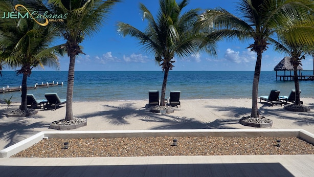 A beach with palm trees, lounge chairs, and a clear view of the ocean. - Tropical 1 Bedroom Cabana on Private Oasis (Maya Beach)