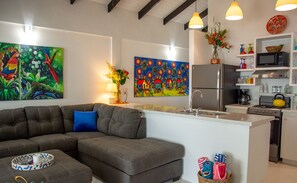 Eine moderne Küche mit grauem Sofa, einem Esstisch und einem farbenfrohen Bild über der Arbeitsfläche.