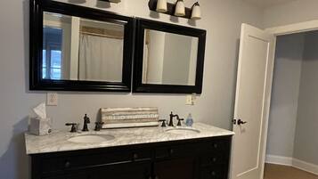 Un bagno con doppio lavabo, due specchi, un lavandino bianco, mobili scuri, un portasciuga e un lampadario sopra gli specchi.