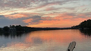 Une jetée en bois, avec un banc et une table, donnant sur une étendue d’eau calme, le ciel se parant des couleurs du coucher de soleil.