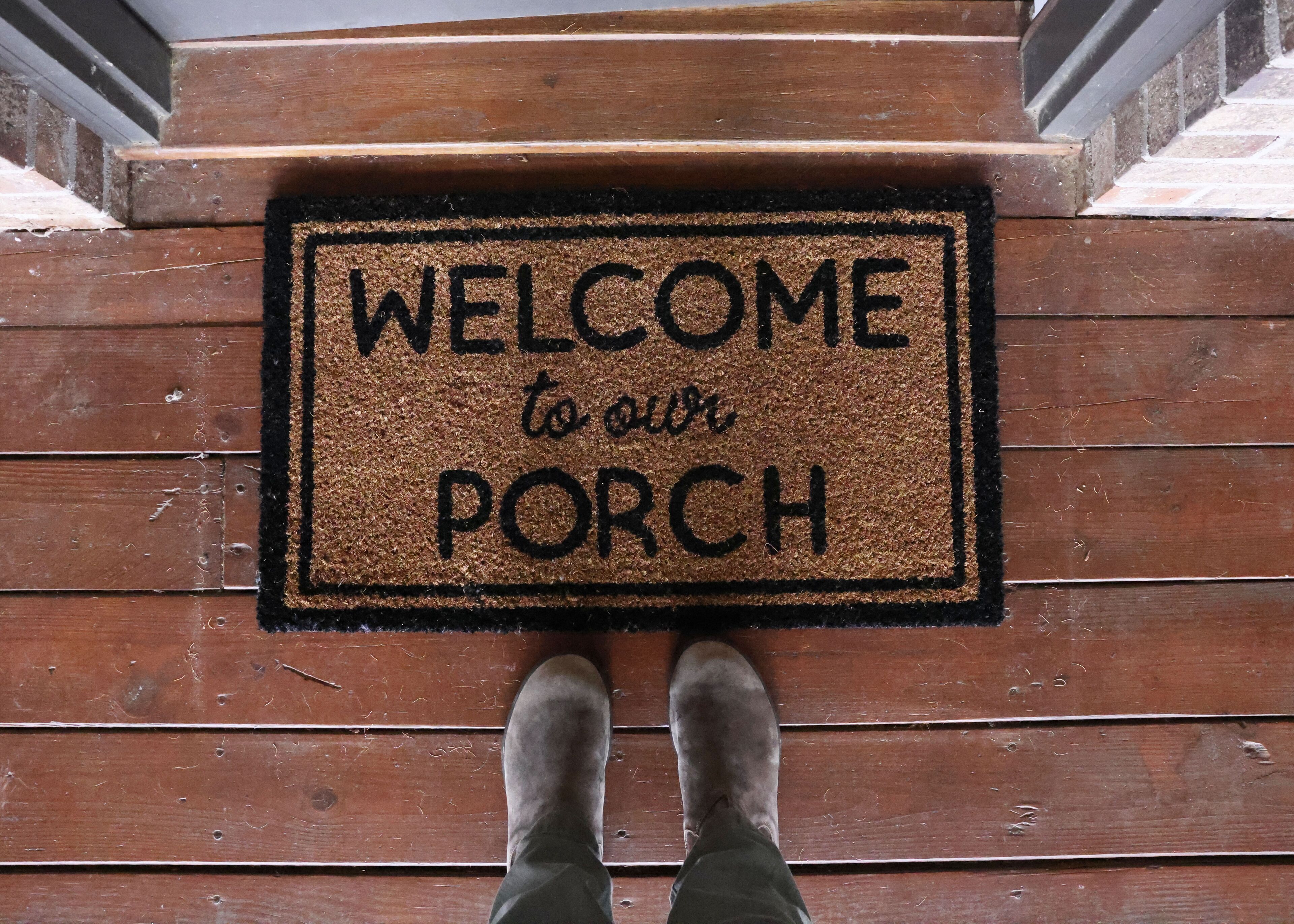 A wooden porch with a welcome mat that reads "WELCOME to our PORCH".
