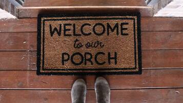 A wooden porch with a welcome mat that reads "WELCOME to our PORCH".