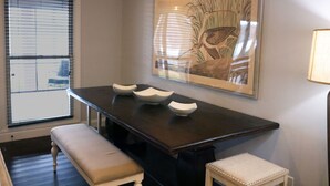 Un coin repas avec une table en bois foncé, trois bols blancs, un banc et une œuvre d’art encadrée accrochée au mur.