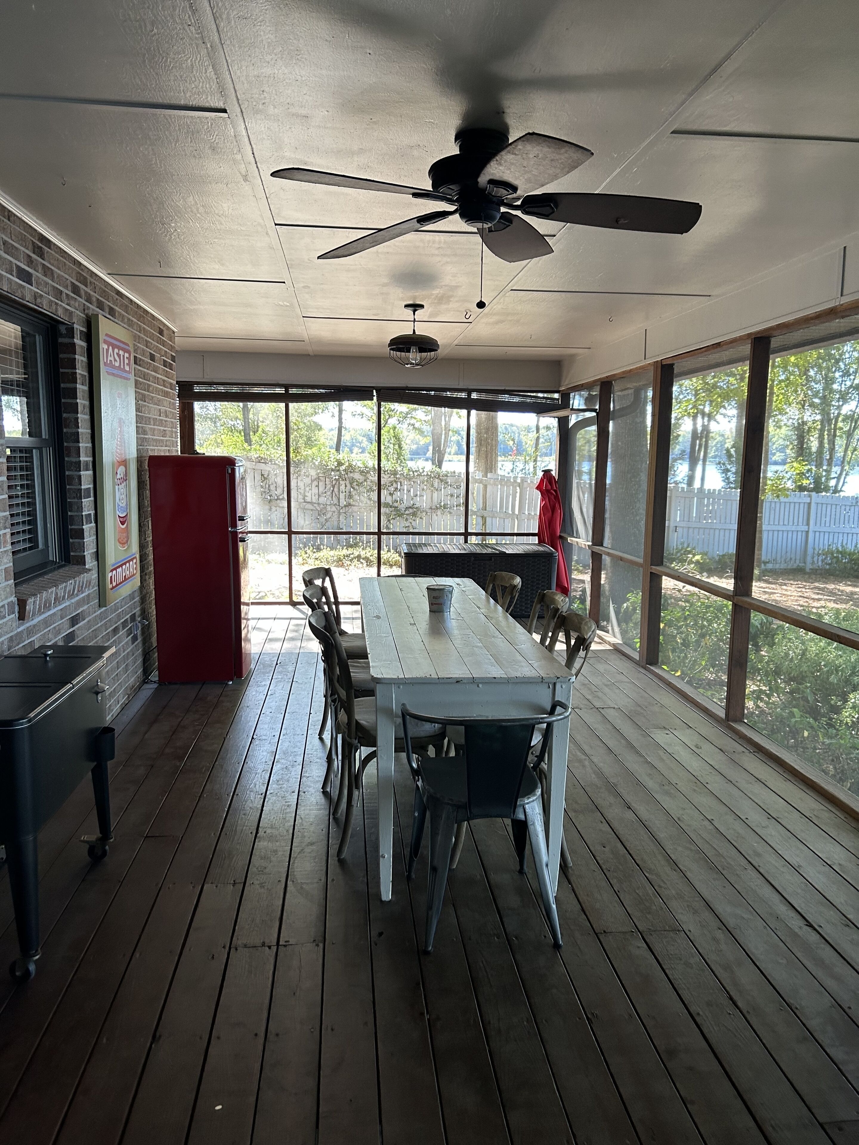 A covered outdoor dining area with a wooden table and chairs, a ceiling fan, and a view of a fenced yard.