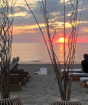 A beach scene with wooden lounge chairs and a sunset.