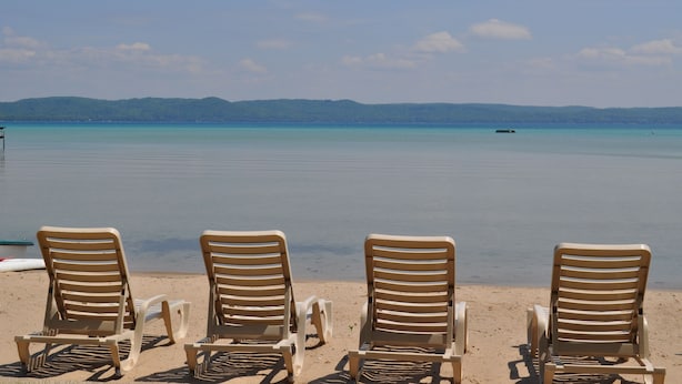 A beach with three sun loungers facing the ocean, a clear sky, and a distant boat.