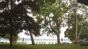 A grassy outdoor area with a view of a lake, surrounded by trees and featuring a picnic table and chairs.