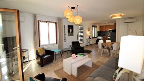 Un soggiorno moderno con divano, tavolino e poltrone. C'è un'area pranzo con tavolo e sedie. La stanza ha una grande finestra e un lampadario.