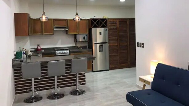 Una cucina moderna con mobili in legno, un frigorifero in acciaio inossidabile e un angolo bar con sgabelli.