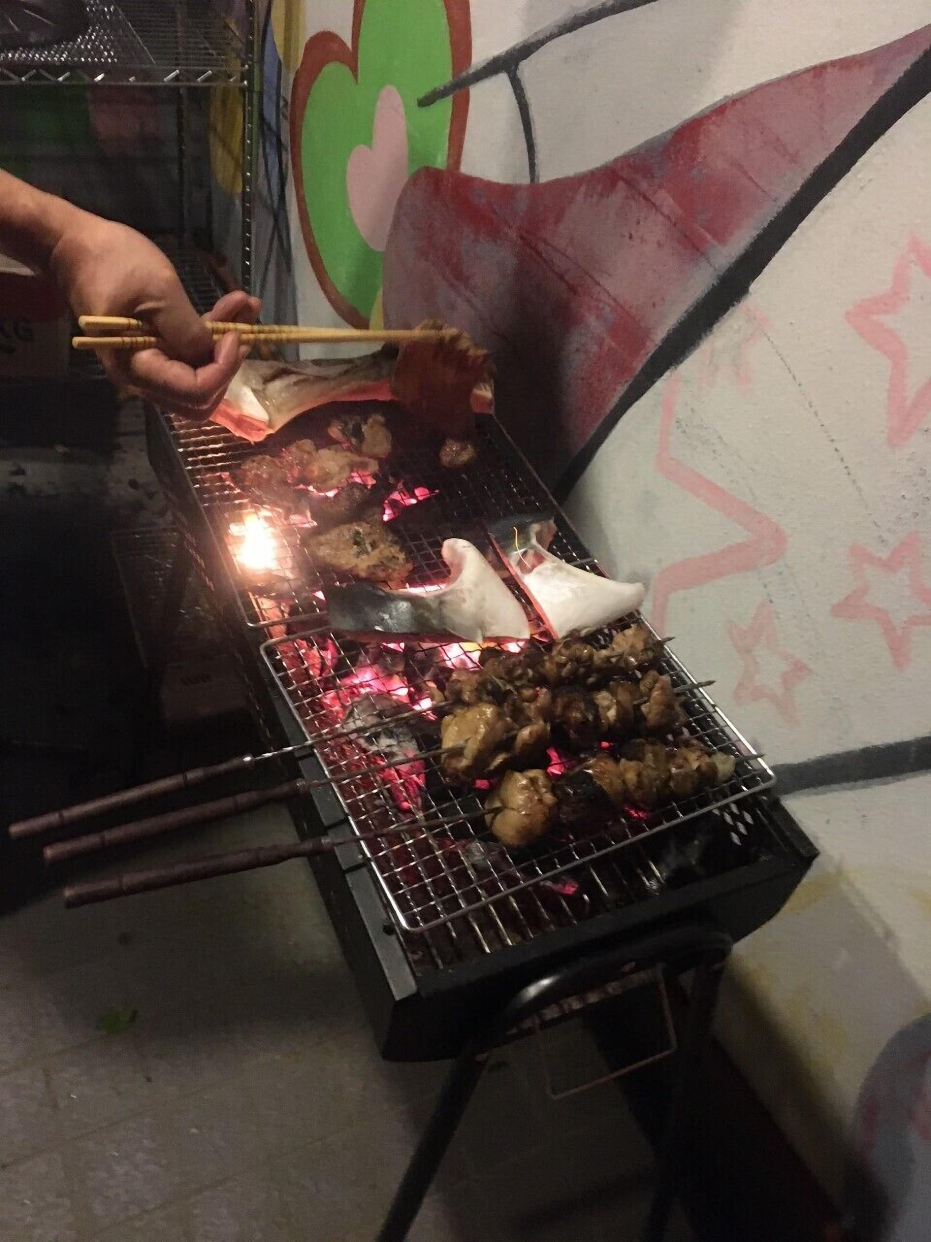 A person grilling food on a portable barbecue with skewers.