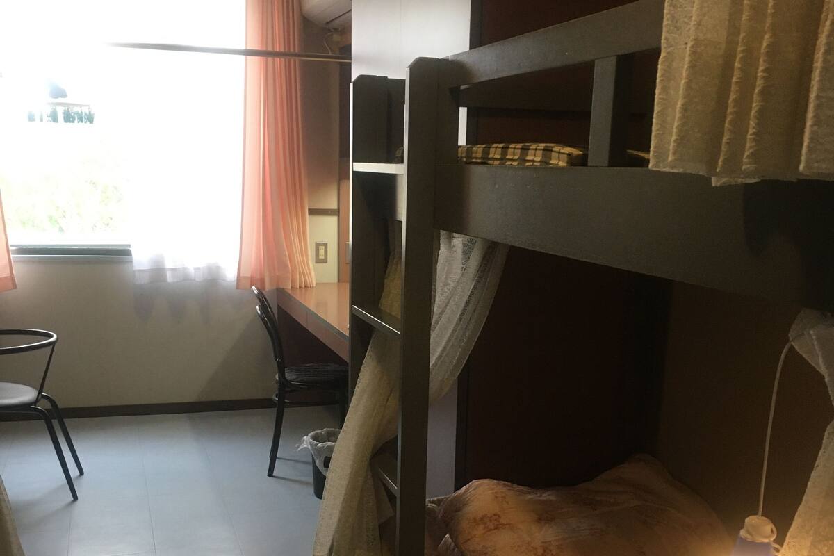 Een slaapkamer met een stapelbed, een raam, een stoel en een tafel.