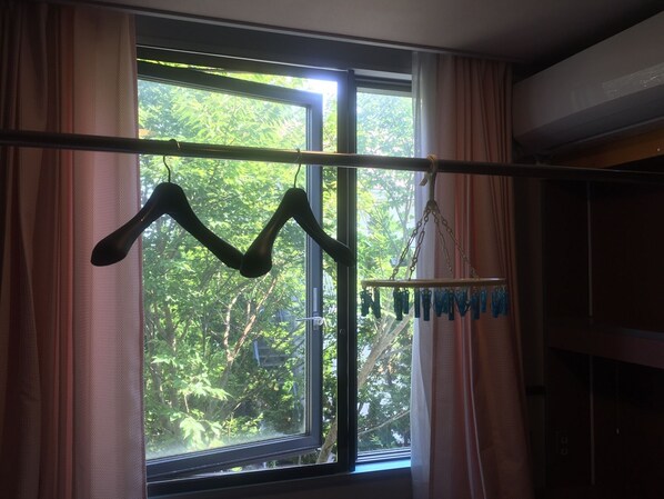 A window with a view of trees, curtains, and a clothing rack with items hanging.