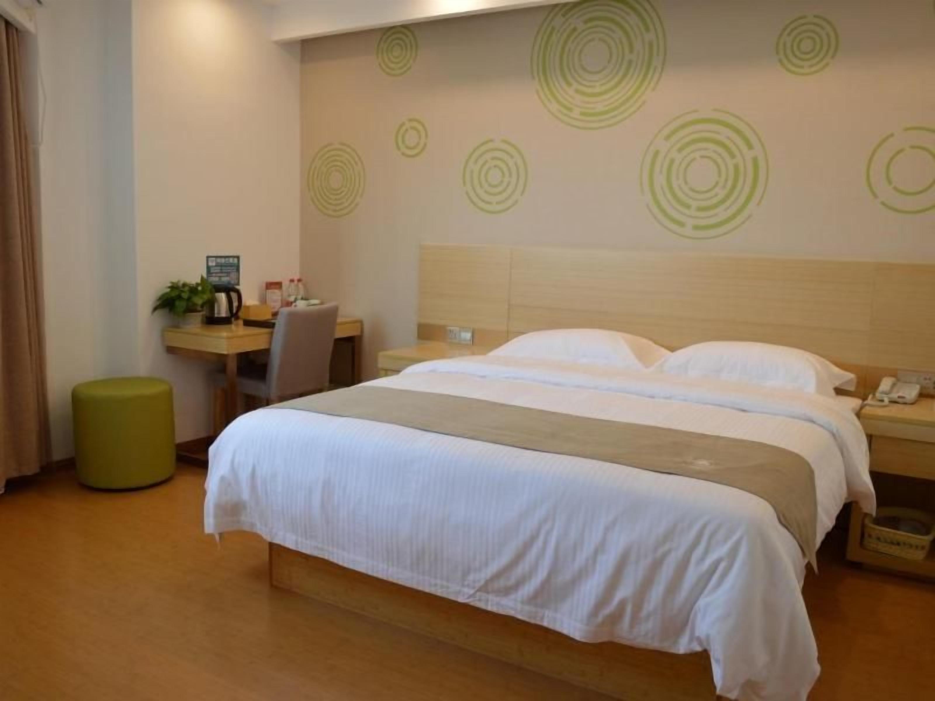 Quarto de hotel com cama, escrivaninha, cadeira, banquinho e parede com desenhos circulares.