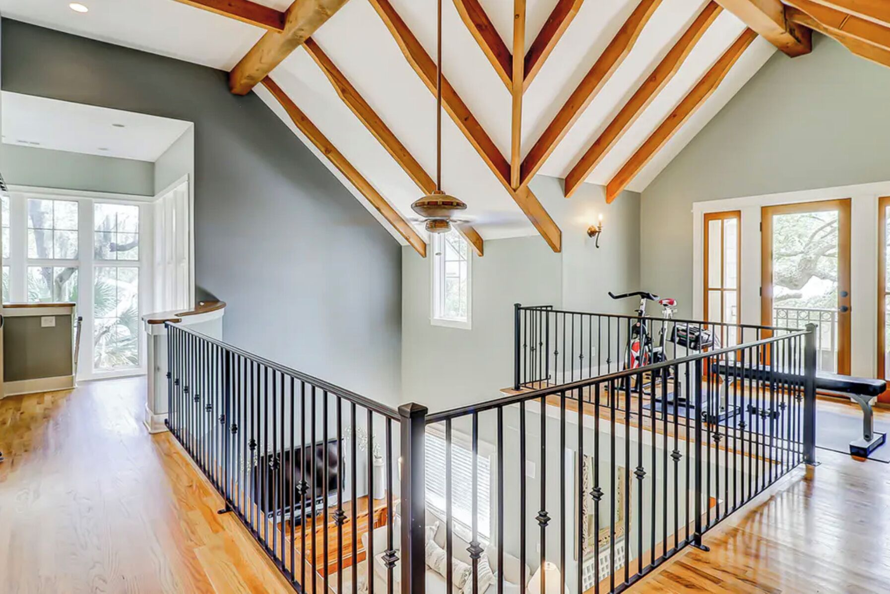 A spacious interior with a high ceiling, wooden beams, and a balcony with exercise equipment.