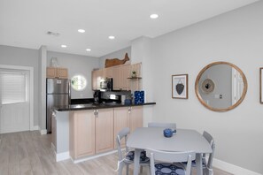 A modern kitchen with light wood cabinets, a stainless steel refrigerator, and a dining area with a round table and chairs.