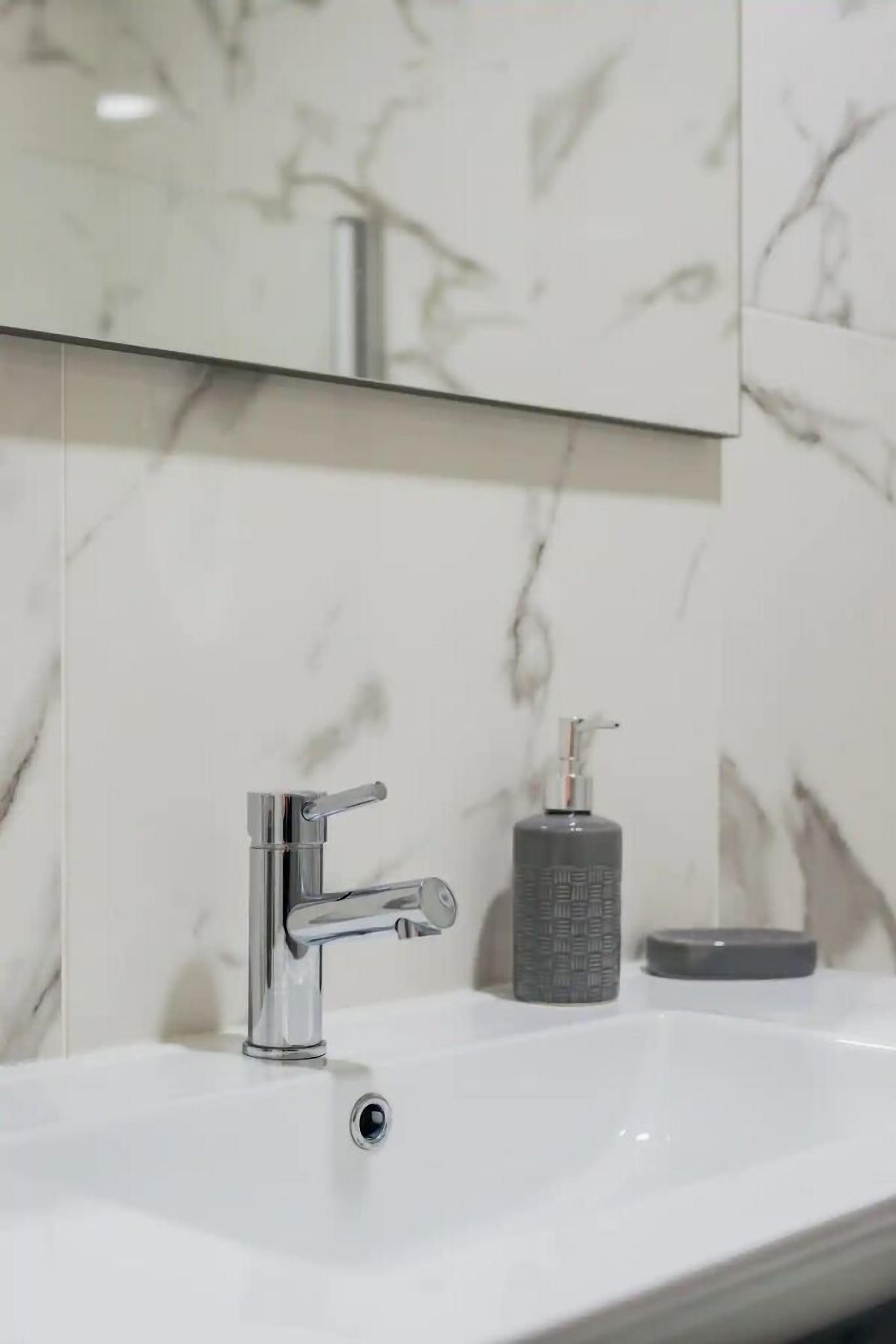 A modern bathroom with a chrome faucet, a soap dispenser, and a mirror above a white sink.