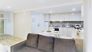 A modern kitchen with white cabinets, a dining area with a table and chairs, and a living area with a sofa. - Imperial Apartment (Braga)