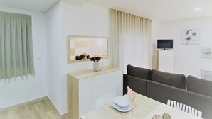 A modern living room with a sofa, a dining table set with plates and a vase of flowers, a TV on a stand, and a mirror above the counter. - Imperial Apartment (Braga)