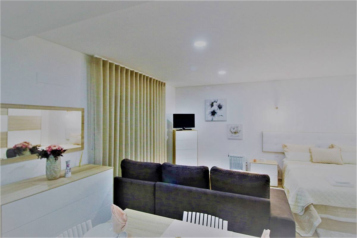 A modern hotel room with a sofa, a TV, a bed, and a bedside table.