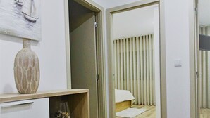 A modern room with a wooden floor, a round woven rug, a white cabinet with decorative vases, and a bed with vertical blinds. - Imperial Apartment (Braga)