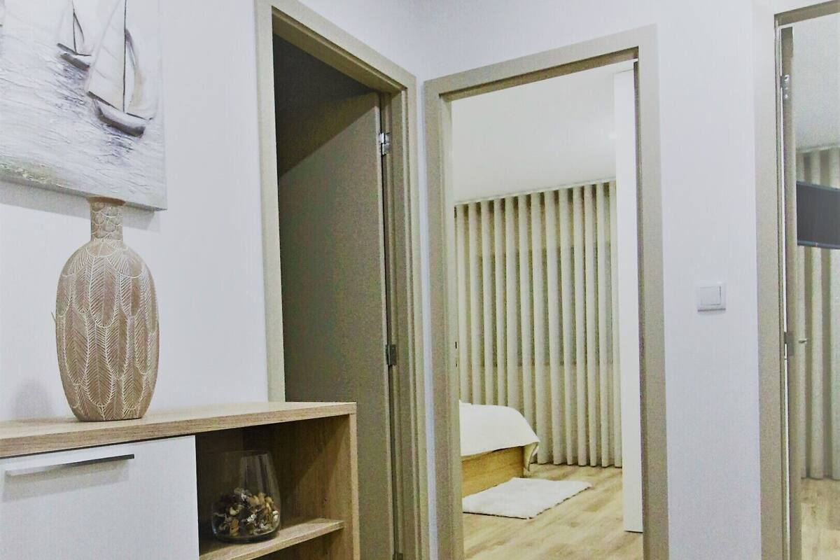 A modern room with a wooden floor, a round woven rug, a white cabinet with decorative vases, and a bed with vertical blinds.