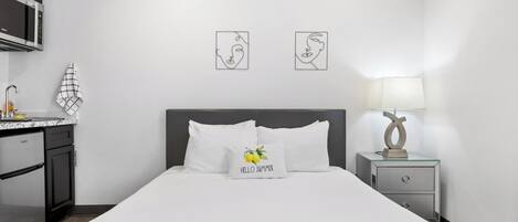 Een hotelkamer met een bed, nachtkastje, lamp, magnetron en een kitchenette.