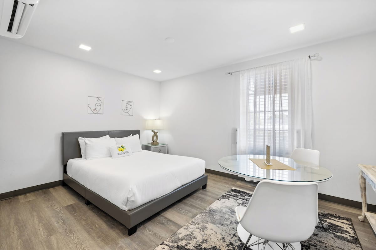 A hotel room with a bed, bedside table, lamp, and a round glass table with chairs.
