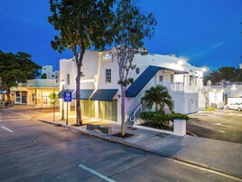 Un hotel moderno con fachada blanca, una entrada visible y un estacionamiento con señal de estacionamiento público.