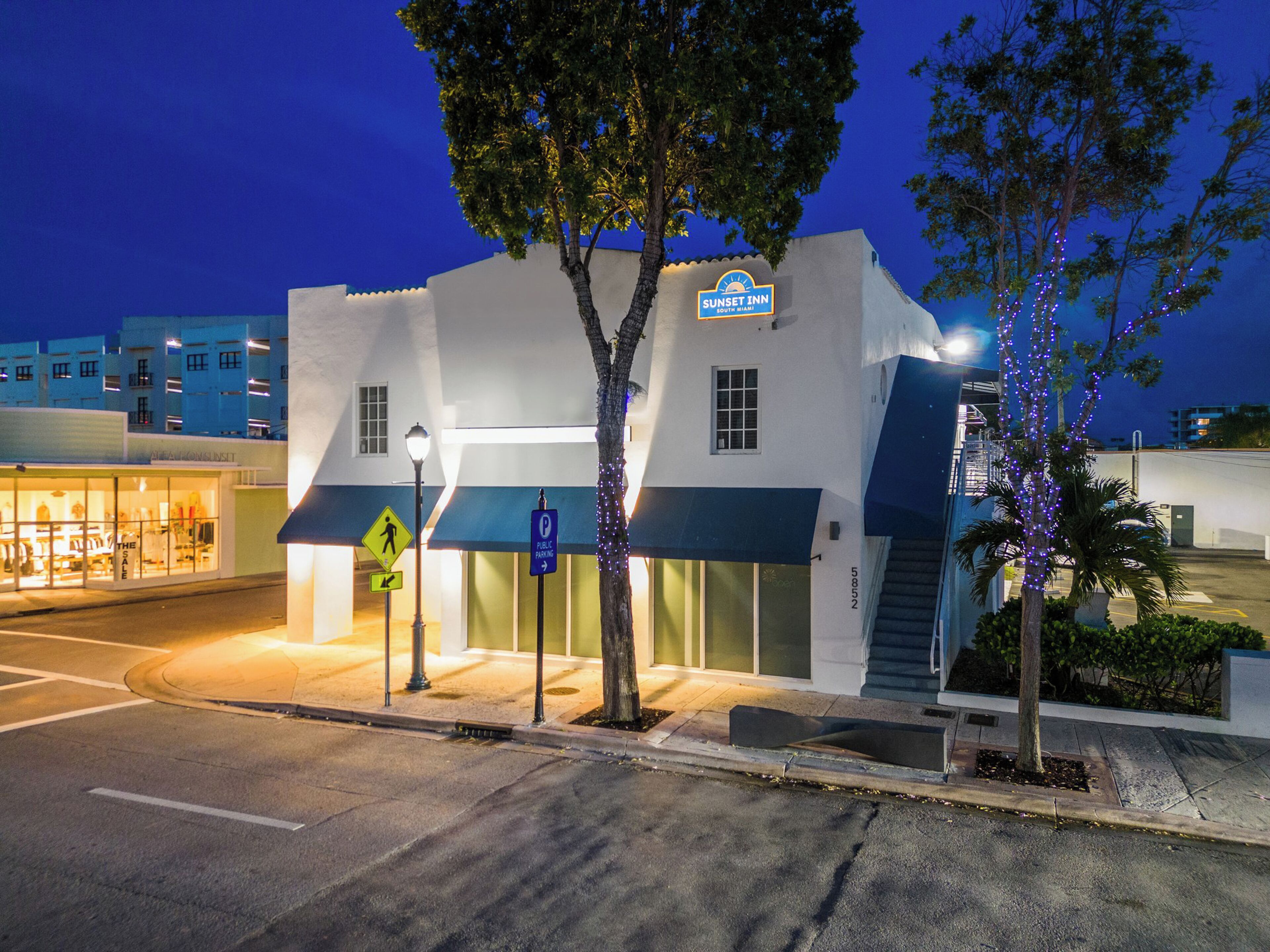 A hotel with a sign reading "Sunset Inn South Miami" and a parking sign indicating public parking.