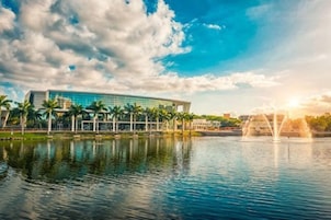 A modern building with a glass facade, a reflective water body, and a fountain.