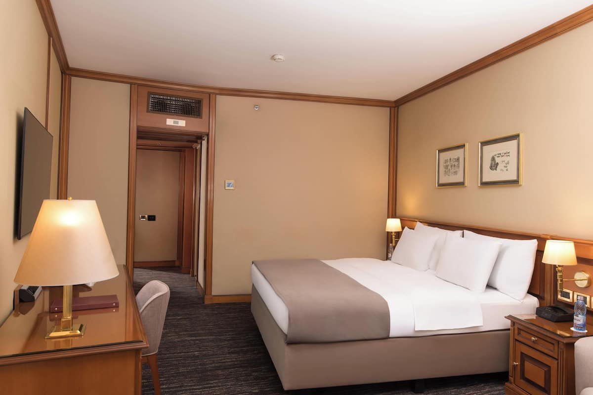 Habitació d'hotel amb llit, taules de nit, escriptori, cadira i una porta que dona a un armari.