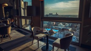 A modern dining area with a table set for two, large windows offering a city view, and contemporary furniture. - Grand Hotel Bucharest (Bucharest)