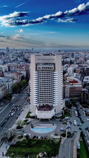 Um hotel alto com uma entrada marcante, cercado por um horizonte urbano e uma rua movimentada.