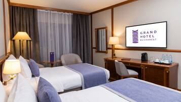 A hotel room with two beds, a desk, a chair, a lamp, a mirror, and a television displaying the hotel name.