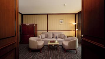 A hotel room with a large sofa set, a wooden cabinet, and a small table with a book.