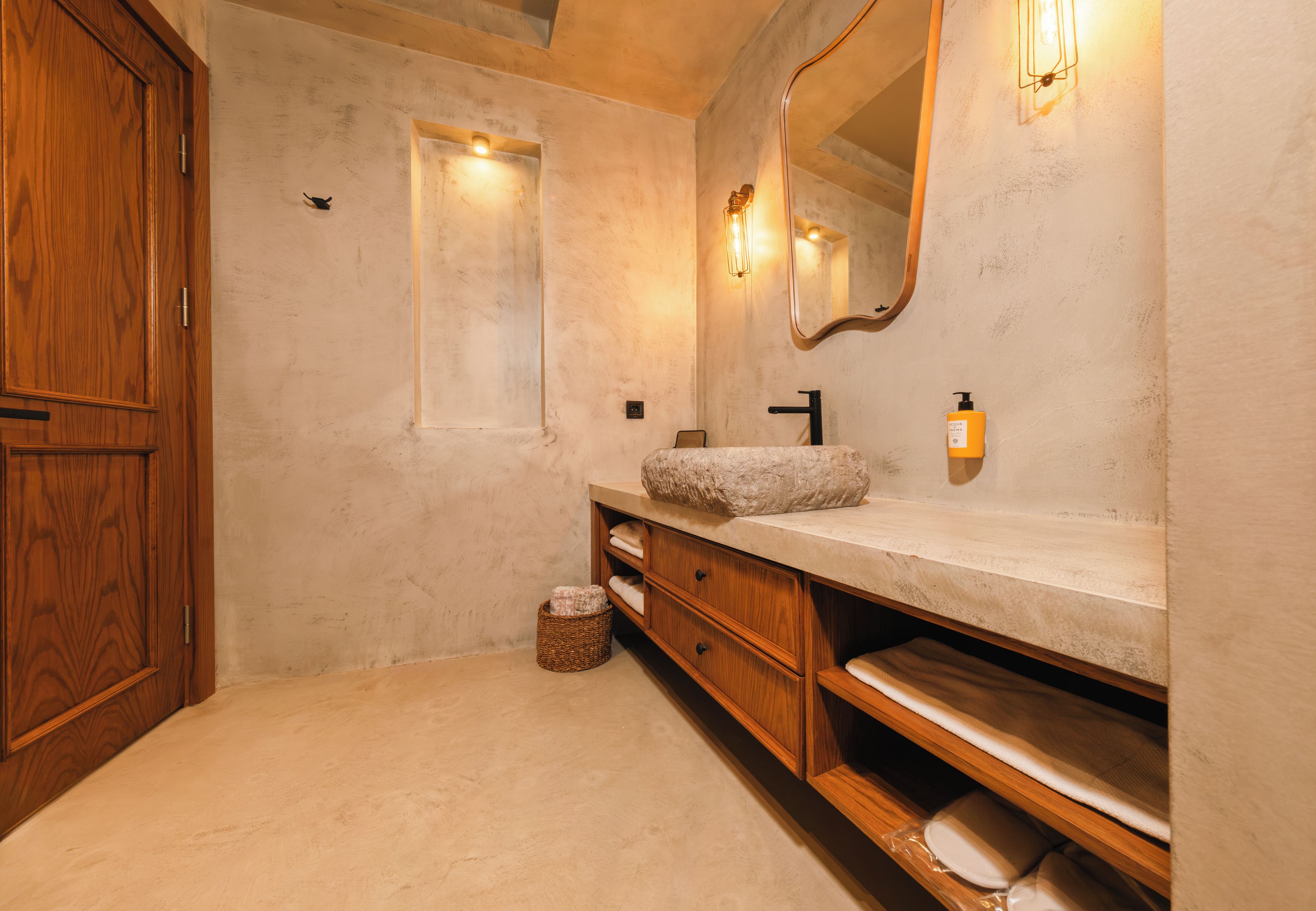 Un baño con tocador de madera, lavamanos de piedra, espejo y una ventana pequeña.