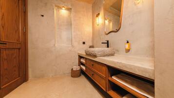 Un baño con tocador de madera, lavamanos de piedra, espejo y una ventana pequeña.