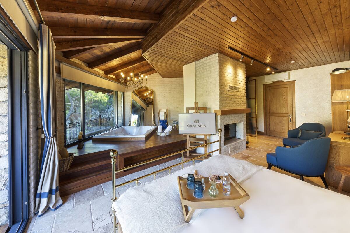 Una habitación amplia con una bañera grande, chimenea y un área de descanso con un sillón azul.
