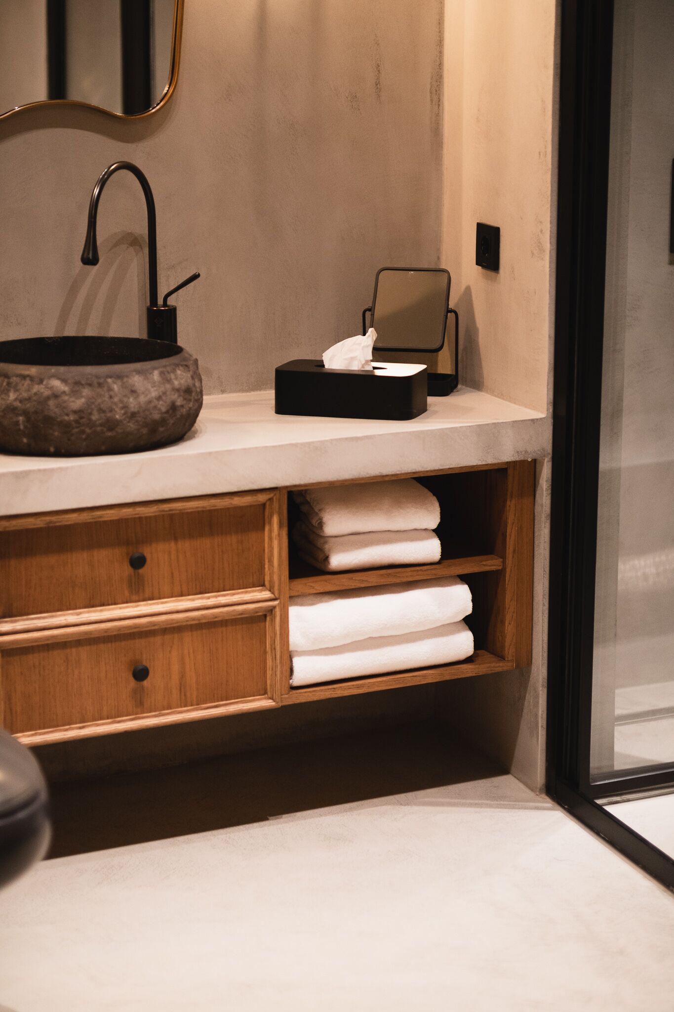 A bathroom with a stone basin sink, wooden cabinetry, and a mirror.